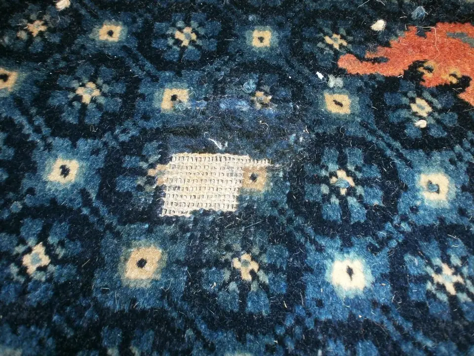 Ein blauer Teppich mit einem Loch im Flor vor der Reparatur